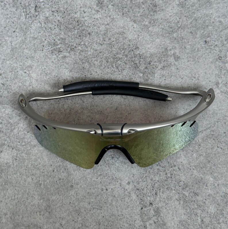 May include: Silver-framed sunglasses with iridescent lenses. The sunglasses have a black nose bridge and ear pieces. The lenses have a gradient of colors, and the frame is a metallic silver color. The sunglasses are designed for sports and outdoor activities.