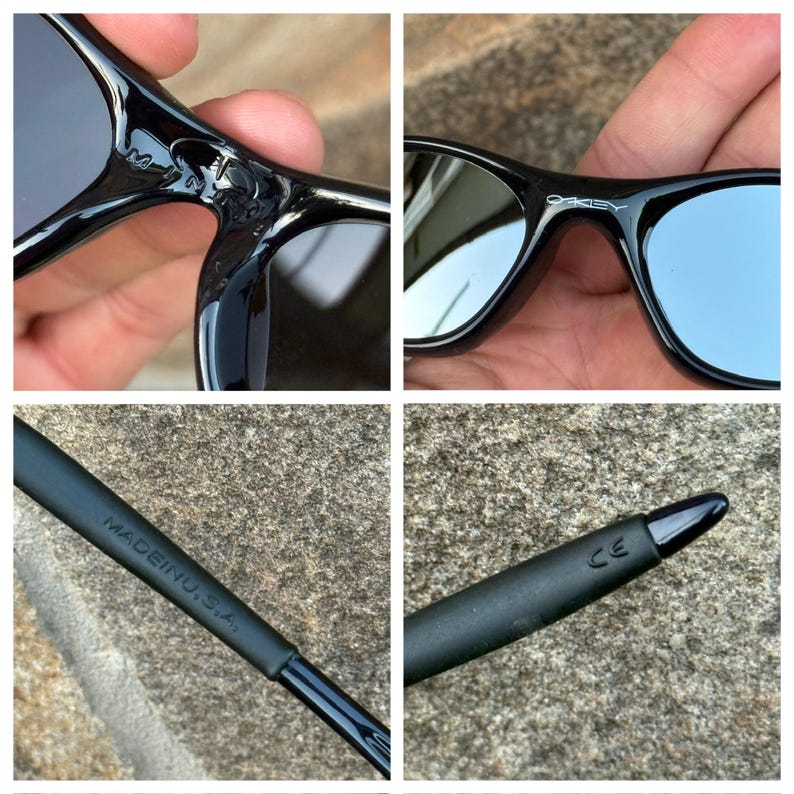 May include: Black sunglasses with mirrored lenses. The frame is glossy and features the brand name "Oakley". The text "MADE IN U.S.A." is printed on the arm. The sunglasses are held in a hand.