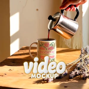 Puede incluir: Una taza beige con diseños florales rosas y el texto "BLOOM where you're planted" se está llenando con un líquido oscuro de una cafetera de acero inoxidable. La taza está sobre una mesa de madera junto a lavanda seca.