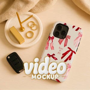 Könnte beinhalten: Eine Handyhülle mit Schleifenmuster und den Worten "love & joy" wird neben einem Autoschlüssel und einem kleinen goldenen Schmuckhalter mit Ringen und einem Lippenstift angezeigt. Die Worte "video mockup" sind ebenfalls sichtbar.