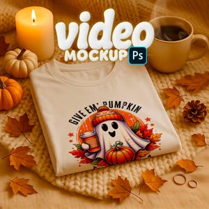 Può includere: T-shirt color crema con grafica a tema autunnale raffigurante un fantasma che tiene una tazza di caffè e una zucca, con la scritta "GIVE EM' PUMPKIN". L'immagine include zucche, foglie, una candela e una tazza di caffè.