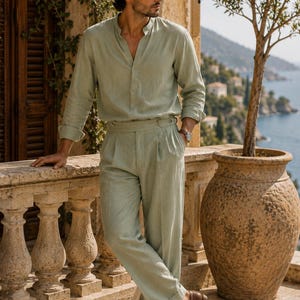 May include: A light sage green long-sleeved shirt with a mandarin collar and matching high-waisted pleated trousers. The outfit is paired with brown leather loafers. The shirt features a button-down front and the trousers have a cuffed hem.