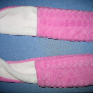 May include: A pink fleece neck warmer with a white fleece lining. The outer fabric has a heart pattern.