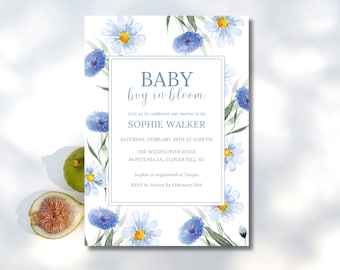 Puede incluir: Una invitación a un baby shower con un diseño floral en acuarela. La invitación tiene un fondo blanco con flores azules y hojas verdes. El texto dice "BABY boy in bloom" e incluye los detalles del evento. Un higo y una rodaja de higo están en la esquina inferior izquierda.