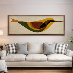 Op de afbeelding: Een ingelijst kunstwerk met een gestileerd vogelontwerp. Het kunstwerk toont een vogel in tinten geel, bruin en groen tegen een beige achtergrond. De lijst is van donker hout. Het kunstwerk hangt boven een witte bank met grijze en geruite kussens.