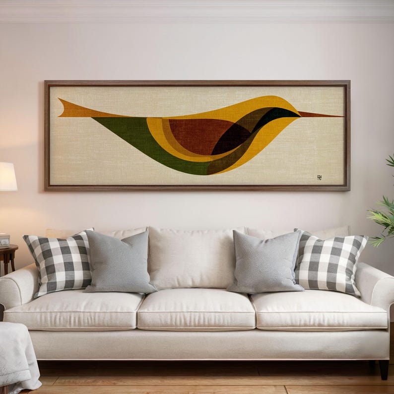 Op de afbeelding: Een ingelijst kunstwerk met een gestileerd vogelontwerp. Het kunstwerk toont een vogel in tinten geel, bruin en groen tegen een beige achtergrond. De lijst is van donker hout. Het kunstwerk hangt boven een witte bank met grijze en geruite kussens.