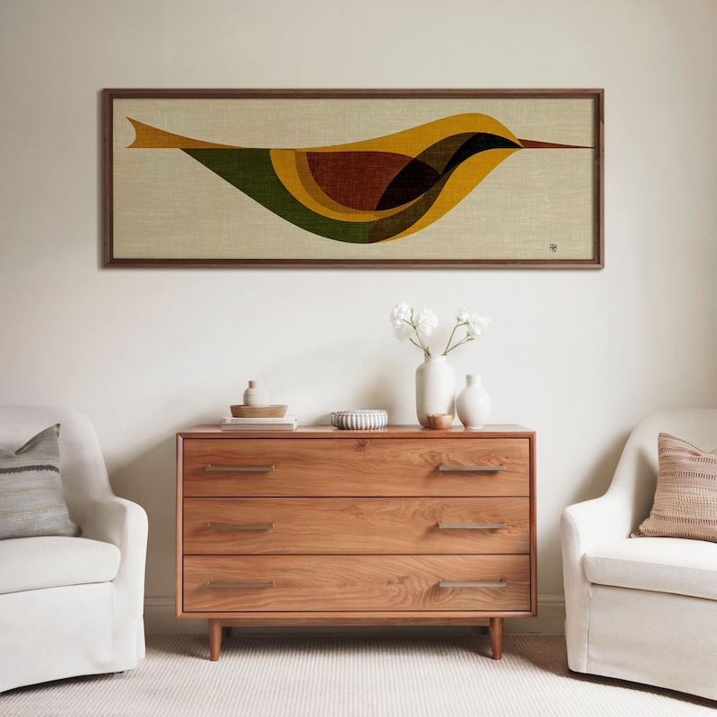 Op de afbeelding: Een ingelijst kunstwerk met een gestileerd vogelontwerp in tinten geel, bruin, groen en zwart. Het kunstwerk is geplaatst tegen een neutrale achtergrond en omlijst in donker hout. Daaronder een houten dressoir met drie lades.