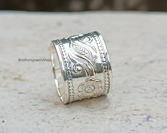 Könnte beinhalten: Ein breiter Silberring mit floralen und Blattmustern. Der Ring weist detaillierte Gravuren von Blumen und Blättern um das Band auf. Der Text "BrothersjewelsShop" ist auf der Seite des Rings zu sehen. Der Ring besteht aus glänzendem, reflektierendem Metall.