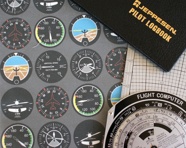 May include: A close-up of a flight computer with a black and white grid pattern. The computer has a dial with numbers and markings for altitude, airspeed, temperature, and fuel. The text "FLIGHT COMPUTER" is printed on the computer.