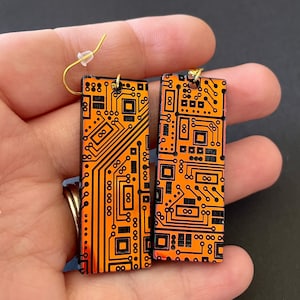 Op de afbeelding: Een paar oranje en zwarte printplaat oorbellen. De oorbellen zijn rechthoekig en hebben een gouden haak.