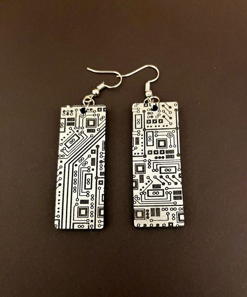 Op de afbeelding: Een paar zilveren oorbellen met een rechthoekig ontwerp met een zwart-wit circuitboardpatroon.