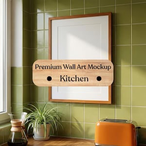 May include: A framed wall art mockup with a wooden frame and a white mat. A wooden sign with the text "Premium Wall Art Mockup Kitchen" is in front of the frame. A small orange toaster and a potted plant are on the counter.