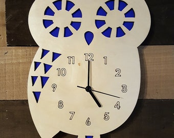 May include: A wooden owl clock with blue accents. The clock face has black hands and white numbers 1 through 12. The owl's eyes are cut out and have a blue background.