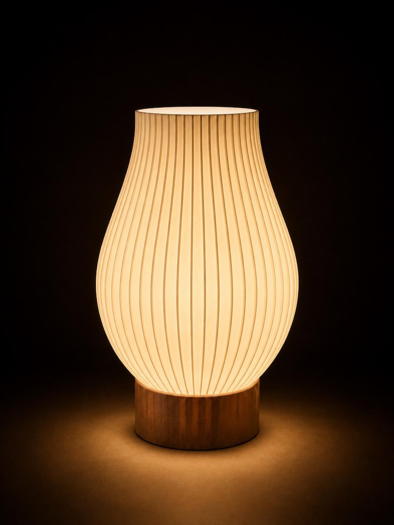May include: A table lamp with a pear-shaped, off-white, vertically ribbed shade that emits a warm, soft glow. The shade is supported by a cylindrical, medium-brown wooden base with a visible grain, creating a contrast between the light and dark elements.