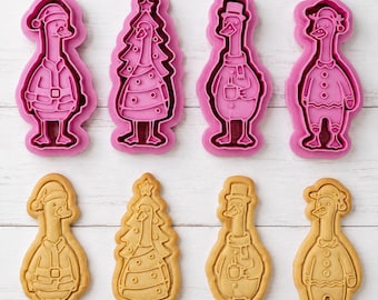 Könnte beinhalten: Ein Set aus vier rosafarbenen Kunststoff-Ausstechformen und vier dazugehörigen hellbraunen Keksen. Die Formen zeigen eine Gans mit Weihnachtsmannmütze, eine Gans in Tannenbaumform, eine Gans mit Zylinder und Schal sowie eine Gans im Schlafanzug.