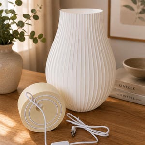 May include: A white, ribbed, vase-shaped table lamp with a rounded base. The lamp features a light-colored, circular wooden base component with a white power cord, a small rectangular inline switch, and a standard USB connector attached to it.