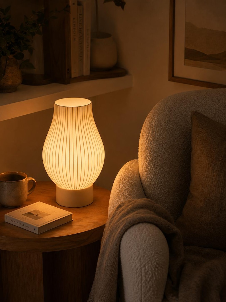 May include: A table lamp with a curved, white, ribbed glass shade that emits a warm, soft glow. The lamp features a solid, cylindrical white base and a slender, tapered neck, providing a diffused light source for a cozy, illuminated atmosphere.