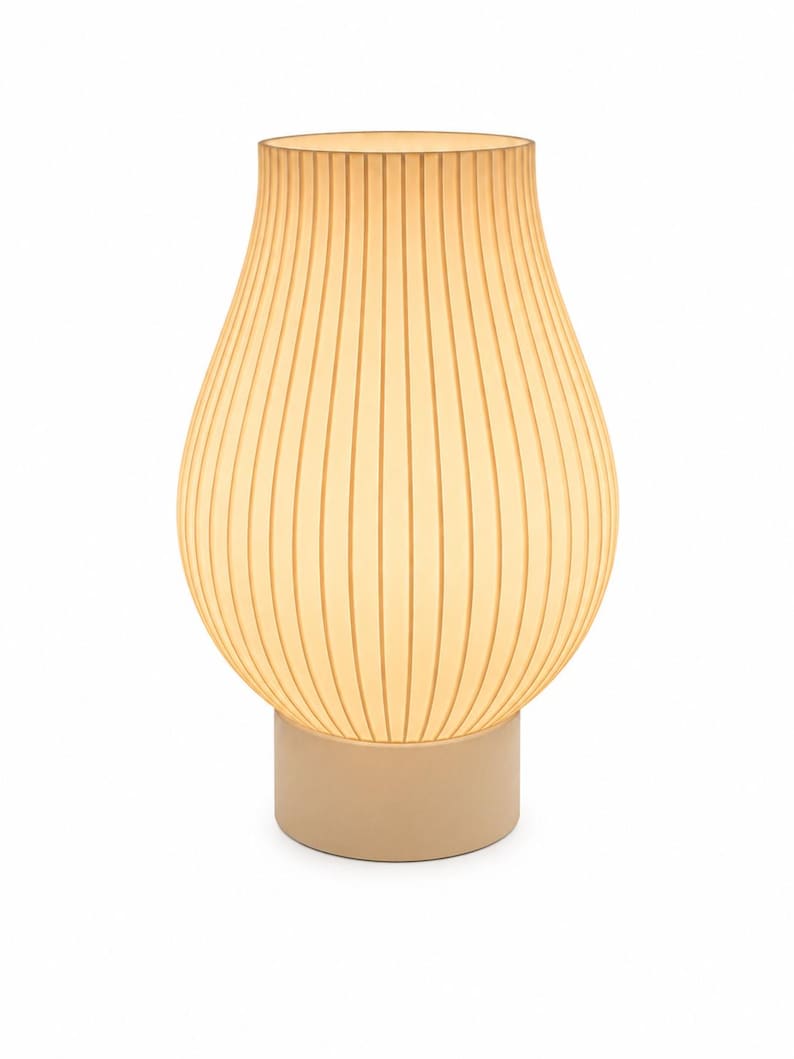 May include: A table lamp with a bulbous, ribbed, translucent cream-colored shade that emits a soft, warm glow. The lamp features a cylindrical, solid cream-colored base that supports the rounded, vertically textured upper section.
