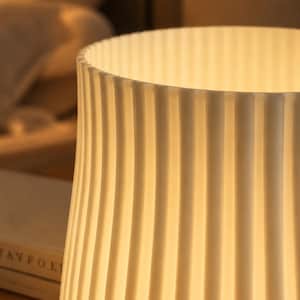 May include: A cylindrical lamp shade with a vertical ribbed texture in an off-white color. The shade is illuminated from within, casting a warm, soft glow through the translucent material, highlighting the repeating pattern of the vertical ridges.
