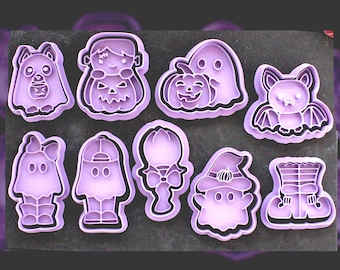 Könnte beinhalten: Ein Set aus neun hellvioletten Kunststoff-Ausstechformen mit verschiedenen Halloween-Motiven, darunter Geister, eine Fledermaus, ein Kürbis, eine Frankenstein-ähnliche Figur, eine Schleife und ein Paar Stiefel, angeordnet auf einer dunkelgrauen Fläche.