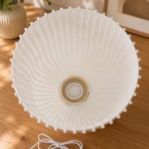 May include: A white, bowl-shaped lamp shade with a ribbed, fluted texture and a scalloped edge featuring small, evenly spaced protrusions. The center contains a circular beige socket fitting, and a white USB power cord is included.