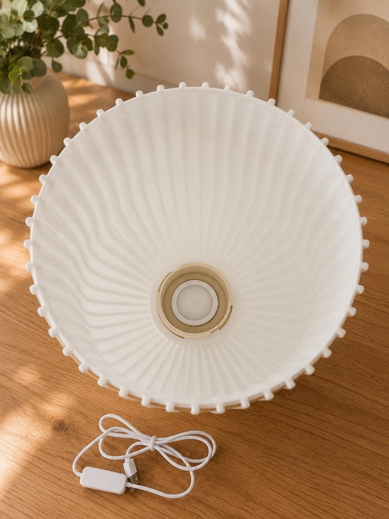 May include: A white, bowl-shaped lamp shade with a ribbed, fluted texture and a scalloped edge featuring small, evenly spaced protrusions. The center contains a circular beige socket fitting, and a white USB power cord is included.
