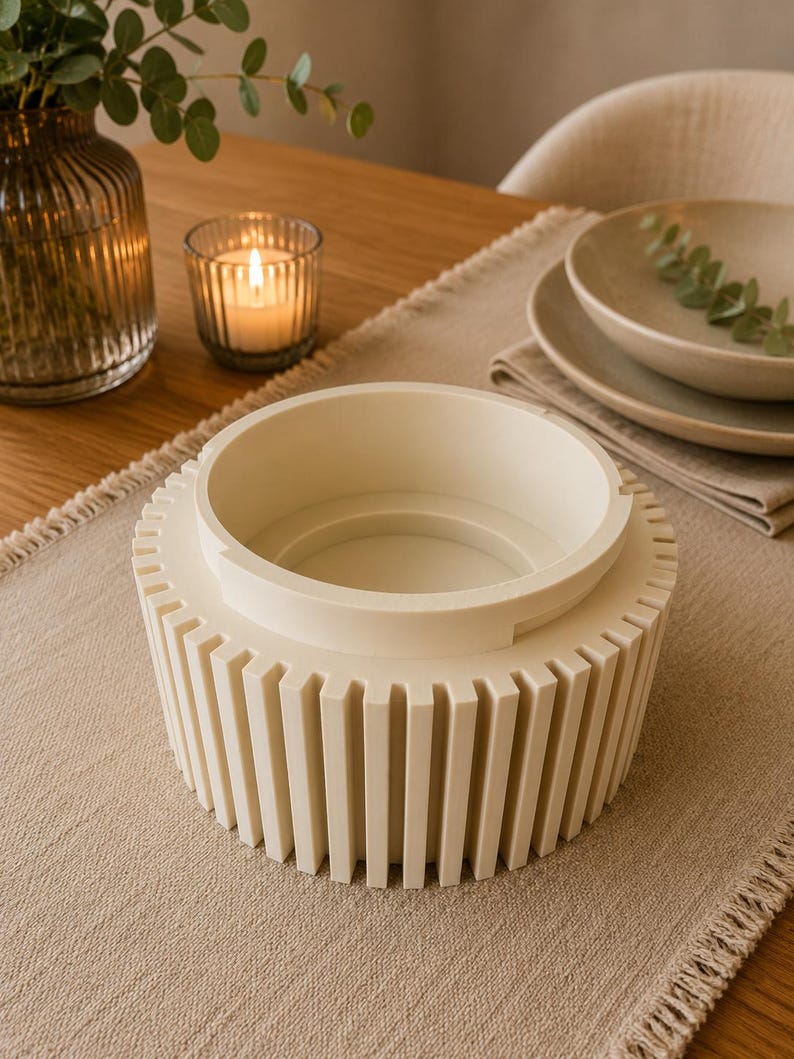 May include: A cream-colored cylindrical bowl featuring a series of vertical, evenly spaced slats around its exterior. The bowl has a smooth, raised inner rim and a flat base, presenting a structured, uniform design with a matte finish throughout.