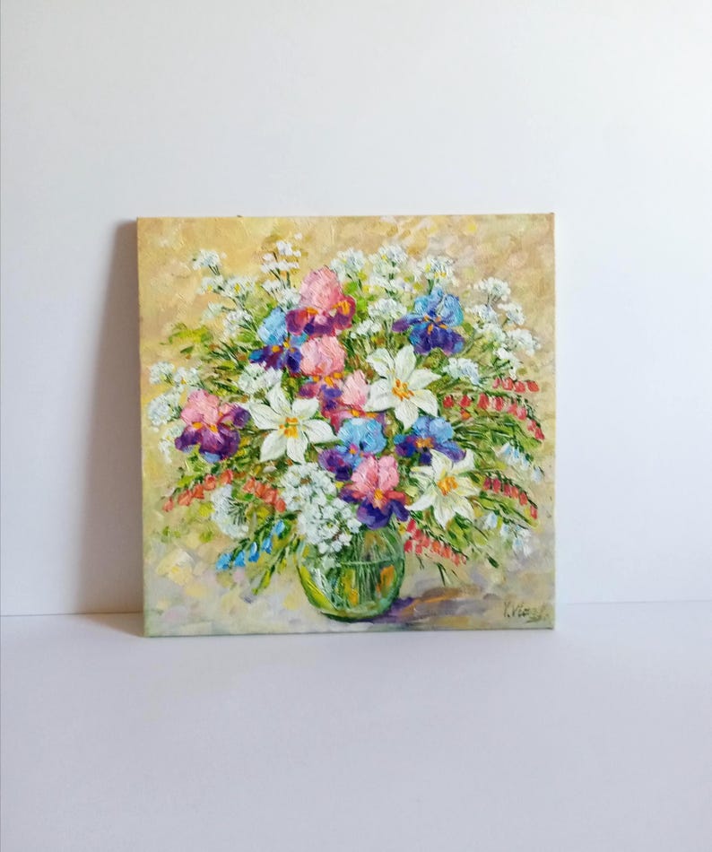 May include: Oil painting of a vibrant floral arrangement in a clear glass vase. The bouquet features white lilies, pink, purple, and blue irises, and small white flowers. The background is a textured, light yellow.