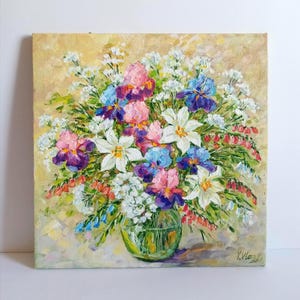 May include: An original oil painting of a floral arrangement in a clear glass vase. The bouquet features white lilies, pink, purple, and blue irises, and small white flowers. The background is a soft yellow with visible brushstrokes.