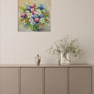 May include: A colorful floral painting featuring a bouquet of white, pink, purple, and blue flowers in a green glass vase. The artwork is displayed on a neutral-toned wall, adding a touch of nature-inspired decor.