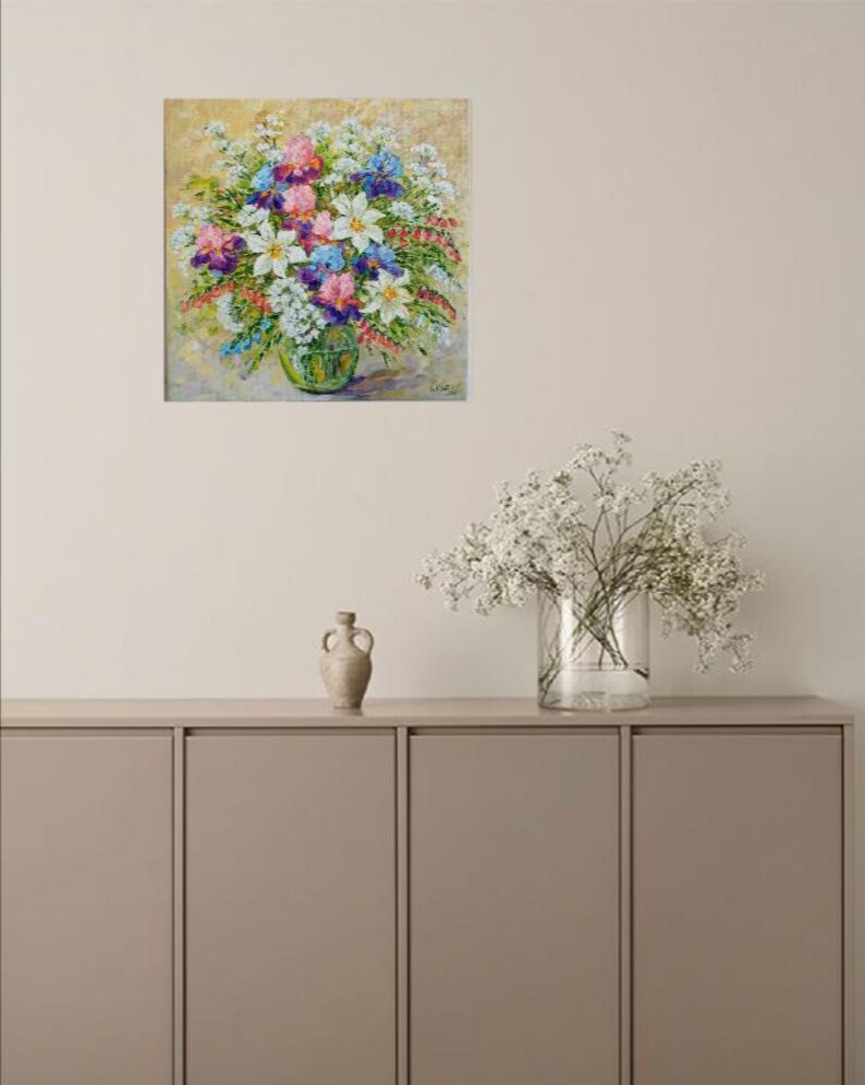 May include: A colorful floral painting featuring a bouquet of white, pink, purple, and blue flowers in a green glass vase. The artwork is displayed on a neutral-toned wall, adding a touch of nature-inspired decor.