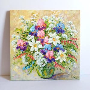 May include: Oil painting of a vibrant floral arrangement in a clear glass vase. The bouquet features irises in shades of purple, pink, and blue, along with white and red flowers. The background is a soft, yellow-toned canvas.