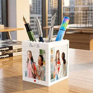 May include: White brick-style pen holder with a photo of a mother and daughter, and the text "Mom & Me". The holder contains a fountain pen, a mechanical pencil, a craft knife, and a rainbow-colored marker. The pen holder sits on a wooden desk.