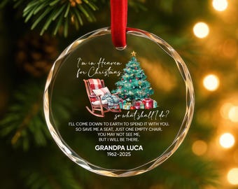 May include: A clear, round Christmas ornament with a red ribbon. The ornament features a Christmas tree, a rocking chair, and text that reads "I'm in Heaven for Christmas." The text also includes the name "Grandpa Luca" and the years 1962-2025.