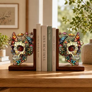 May include: A pair of bookends featuring stained glass style skulls adorned with colorful butterflies and mushrooms. Each skull is mounted on a dark wooden base, supporting a row of four books titled The Kinfolk Home, Live Beautiful, The Studio, and Scandi Rustic.