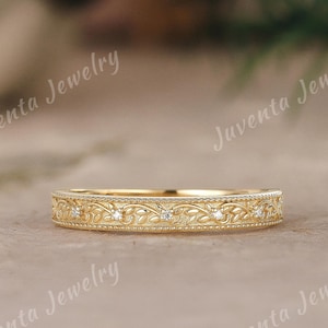 Pode incluir: Um anel de banda em ouro amarelo com um intrincado padrão gravado de folhas e vinhas na superfície exterior, acentuado com pequenas pedras redondas transparentes espaçadas. O texto Juventa Jewelry é visível no fundo.