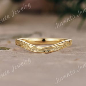 Può includere: Un anello color oro con un design curvo. L'anello presenta un motivo floreale inciso sulla parte superiore. L'anello è di Juventa Jewelry.