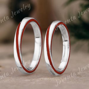 May include: Two silver rings with a vibrant red enamel inlay. The rings are set against a neutral background, with the text "Juventa Jewelry" subtly visible. The rings are likely wedding bands or fashion accessories.