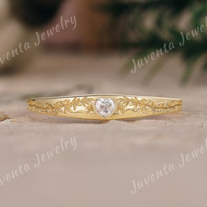 May include: A gold ring featuring an engraved leaf pattern along the band and a single heart-shaped clear gemstone set in the center. The text Juventa Jewelry is visible in the image. The ring has a polished finish and a tapered design.