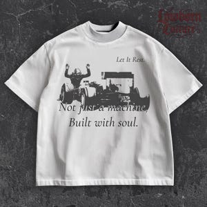 May include: White short-sleeve t-shirt with a mock neck collar. The shirt features a black and white graphic of a race car and driver, with the text "Let It Rest." and "Not just a machine, Built with soul."
