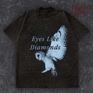 May include: Dark gray t-shirt featuring a white and blue owl graphic with the text "Eyes Like Diamonds." The owl is depicted with outstretched wings against a starry background. The shirt has a vintage, worn look.