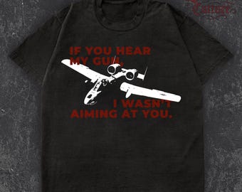 Puede incluir: Camiseta negra con un diseño blanco de un avión militar y el texto rojo "IF YOU HEAR MY GUN, I WASN'T AIMING AT YOU". La camiseta tiene cuello redondo y mangas cortas. El tejido tiene un aspecto desgastado.