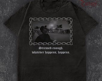 May include: Dark grey t-shirt with a black and white image of a person in a chain-linked frame. The text "Stressed enough. whatever happens, happens." is printed below the image. The shirt has a crew neck and short sleeves.