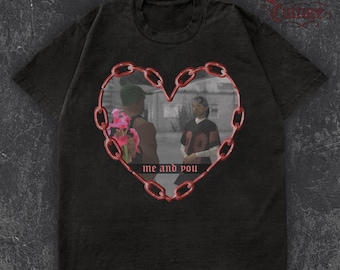 May include: Black t-shirt with a heart-shaped chain design. The design features a grayscale image of two people, framed by a red chain, with the text "me and you". The shirt has a vintage appearance.