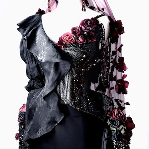 May include: A gothic-style black dress with a ruffled bodice and a sequined corset. The dress is adorned with burgundy roses and a matching headpiece with a veil. The overall design is dark and dramatic, suitable for themed events.