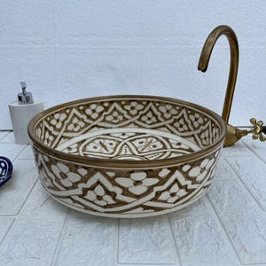May include: A decorative ceramic sink with a brown and white floral pattern. The sink has a round shape and is paired with a brass faucet. A white soap dispenser is visible on the left.