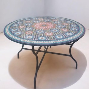 Könnte beinhalten: Ein runder Mosaiktisch mit schwarzem Metallrahmen. Die Tischplatte hat ein farbenfrohes Muster aus blauen, grünen und roten geometrischen Formen. Der Tisch hat einen Durchmesser von etwa 122 cm.