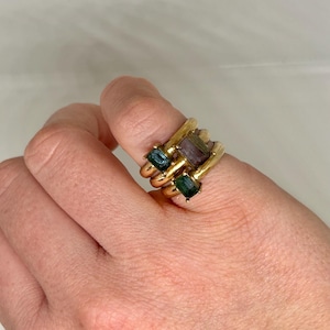 Può includere: Tre anelli d'oro impilati, ognuno con una gemma rettangolare. Le gemme sono nei toni del verde acqua, viola e verde. Un gioiello unico.