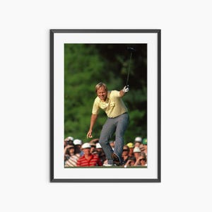 Puede incluir: Impresión enmarcada de un golfista con camisa amarilla y pantalones a cuadros, en pleno swing, con un palo de golf levantado. Una multitud de espectadores es visible en el fondo, con follaje verde. La imagen está en un entorno natural.