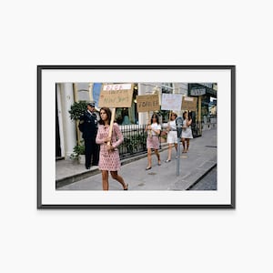 Puede incluir: Una fotografía vintage muestra a un grupo de mujeres manifestándose en la calle, sosteniendo carteles. Los carteles dicen "Dior Unfair Mini Skirts" y "Mini Skirts Forever". Las mujeres visten minifaldas y vestidos. Se ve a un oficial de policía.
